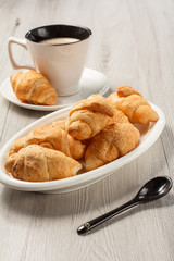 Fresh croissants on white porcelain dish, cup of black coffee with saucer