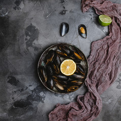 top view of delicious mussels with shells on vintage plate and lime with lemon and cloth on grey