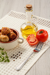 Fried meat cutlets in ceramic soup bowl, red tomatoes, glass bottle with sunflower oil, metal fork and black peppercorn