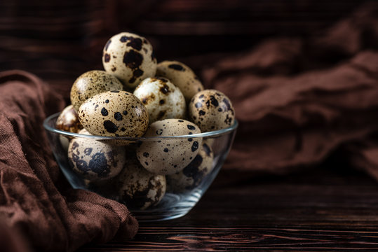 Quail eggs in a glass transparent mug with brown napkin  on a wooden background