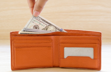 Hand stealing out money from wallet on wooden table.