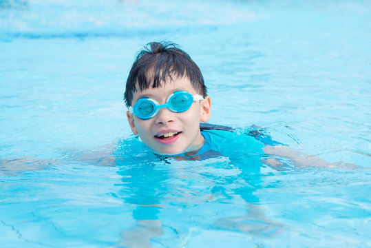 Young asian boy wearing goggles swimming in outdoor swimming pool