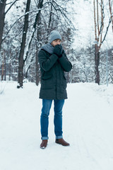 Fototapeta na wymiar young man warming hands up while walking in snowy park