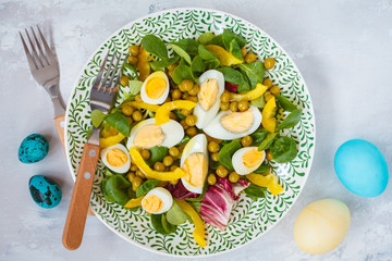 Spring Easter salad with chicken and quail eggs, lettuce corn, pepper, painted eggs. Top view, copy space. Easter concept.