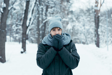 Fototapeta na wymiar portrait of young man warming hands up while walking in snowy park