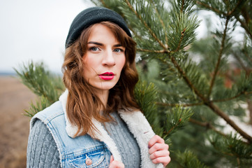 Portrait of brunette girl in hat and jeans jacket at christmas tree.