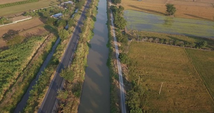 High angle view, Aerial view from drone flight Irrigation canal, beside two paddy fields and road rural scene Thailand. Morning sunrise time