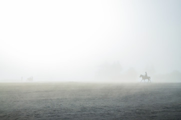 An Asian man is riding a horse in the desert with foggy sky. Space for text