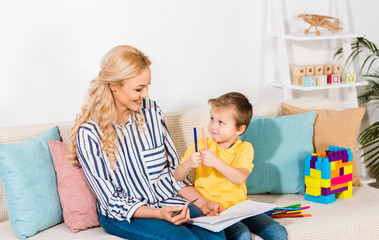 young mother and son drawing picture together while resting on sofa at home