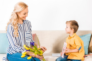 Naklejka premium son gifting smiling mother bouquet and postcard on mothers day