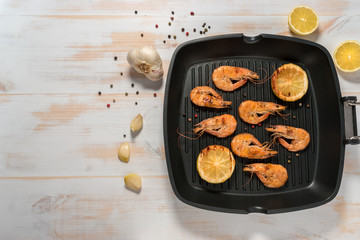 Grilled shrimps on a grill frying pan with lemon, paprika, spices and herbs. Wooden background.