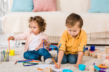 adorable siblings playing on a floor with colored pencils