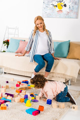 smiling pregnant mother looking how daughter playing with toys