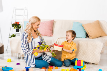 little boy presenting to smiling pregnant mother tulip flowers and heart shaped gift box