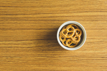 Mini pretzels in white bowl on the wooden table.