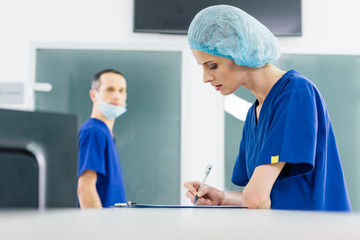 female surgeon writing diagnosis while colleague looking at her in hospital