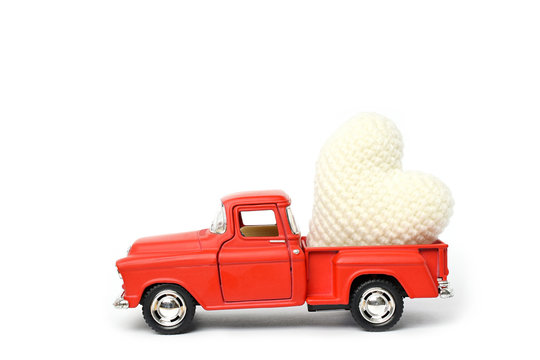 Red toy car delivering white heart for Valentine's day on white background