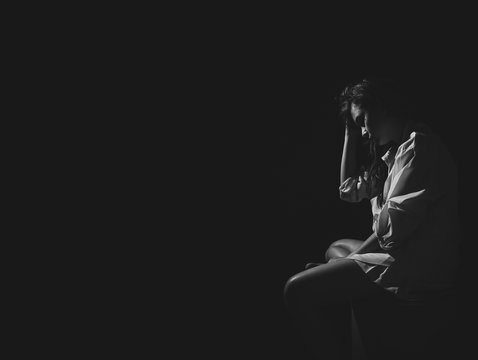 The Depression Woman Sit On The Chair On Dark Background, Sad  Asian Woman Silhouette In Dark, Monochrome Image. Free From Copy Space.