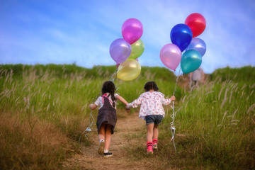 kids running to the meadow on thi hills with holding in hand multicolor ballons