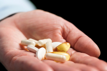 Woman take in the hand variety medication pills, yellow capsules of omega 3, glucosamine and calcium dietary supplements in the palm hand on black background