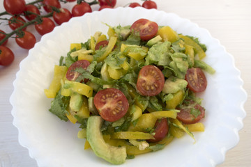 Appetizing vegetable salad consisting of tomatoes, avocado, yellow sweet pepper, lettuce and seasonings and cherry tomatoes on a branch.