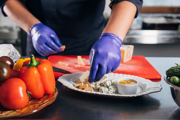 cropped shot of chef putting cheese slices on plate