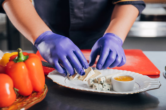 cropped shot of chef putting cheese slices on plate at restaurant