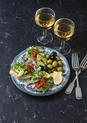 Mediterranean style antipasto and wine. Smoked salmon, avocado, arugula bruschetta, olives and two glasses of white wine on dark background