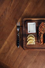 top view of grilled salmon steak served on wooden board with lemon slices