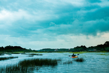 alone man canoeing in the outdoor lake of south carolina marsh with dramatica cloudy sky