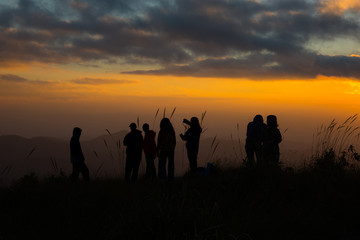 Fototapeta na wymiar Silhouette A group of trourist standing on peak of mountains and enjoy to see beautiful landscape view of sunset, hiking tourist adventure on vacation on mountains 