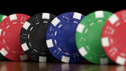 Poker chips stand in a row on a black background, a Domino effect. Playing poker chips are on the table, a symbol of casino