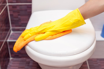 Woman in yellow rubber gloves cleaning toilet seat cover with orange cloth. Bathroom and toilet...