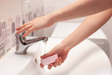 A woman takes a soap and opens a water tap to wash her hands in a white sink in the bathroom