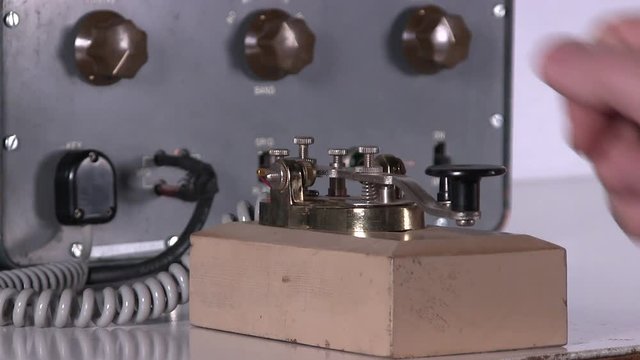 Close-up of hand typing out morse code message with telegraph key over radio station broadcast transmission on vintage electronic hardware engineering military lab test equipment device