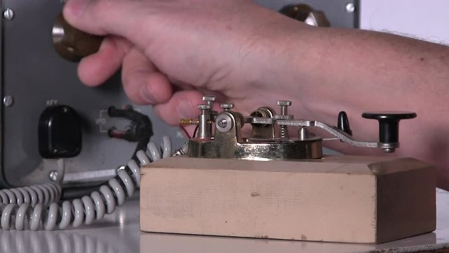 Morse code telegraph operator makes adjustments then types out message with telegraph key over radio station broadcast on vintage electronic hardware engineering military lab test equipment device