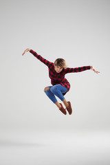Delighted young girl in casual clothes jumping at studio