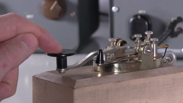 Close-up of finger typing morse code with telegraph key over radio station broadcast transmission on vintage electronic hardware engineering military lab test equipment device in the background