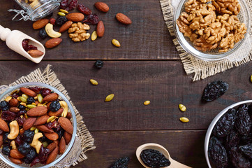 Many different nuts (almonds, cashews, walnuts), dried berries (blueberries, cranberries), prunes, pumpkin seeds in bowls on a dark wooden background. Antioxidant product. Healthy food.