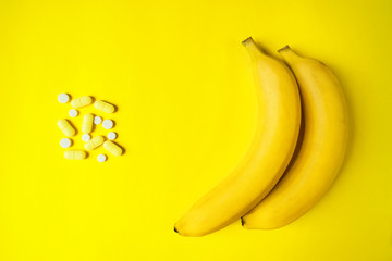 Bananas and pills on a yellow background. The concept of health: the choice between tablets and...