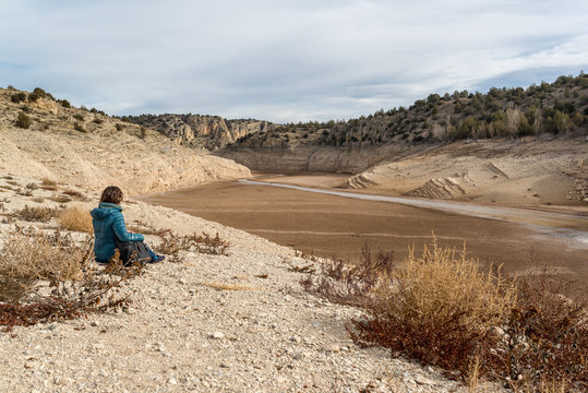 Mujer sentada mirando a un embalse sin agua debido a una sequ&iacute;a prolongada en Espa&ntilde;a. Cambio Clim&aacute;tico. 