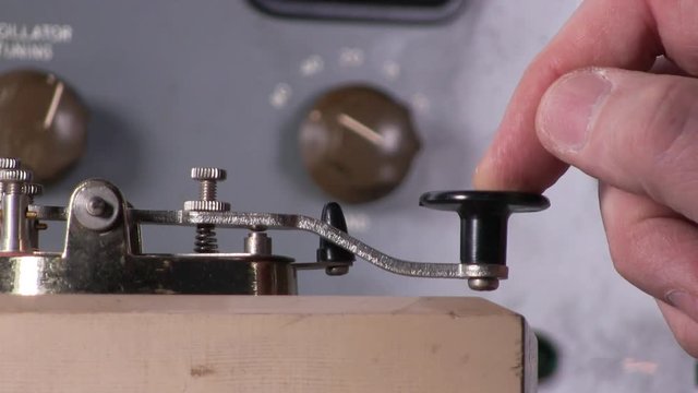 Extreme close-up of finger pressing telegraph key to send morse code radio transmission with vintage electronic hardware engineering military lab test equipment device in the background