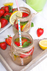 Mineral  water with fresh strawberries, lemon  and mint in jar on a white wooden background, copy space