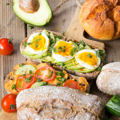 Kanapka z awokado i jajkiem gotowanym na miękko i pomidorem na drewnianym tle. Świeże, organiczne i zdrowe śniadanie.