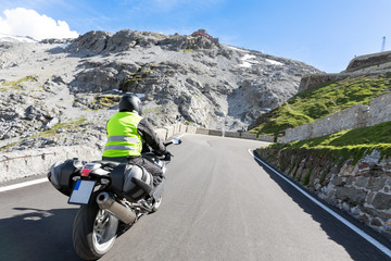 Motorradfahrer fährt mit seinem Motorrad auf kurvigen Straßen durch die Berge und einer...