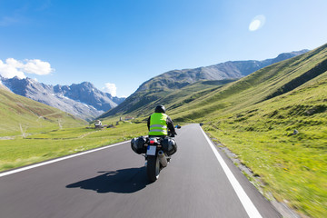 Fototapeta premium Motorbiker is riding his motorcycle on winding roads through the mountains an beautiful landscape