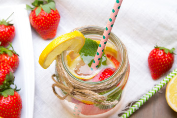 Mineral  water with fresh strawberries, lemon  and mint in jar on a white wooden background, copy space