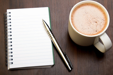 Blank notebook, pen and cup of coffee on wooden brown background, copy space.