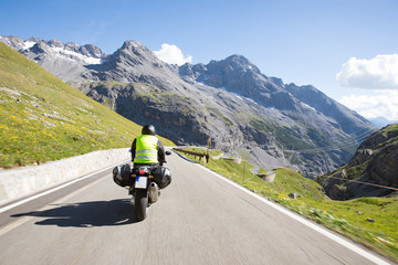 Motorradfahrer fährt mit seinem Motorrad auf kurvigen Straßen durch die Berge und einer wunderschöne Landschaft © Merpics