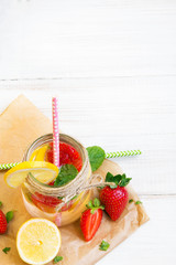 Mineral  water with fresh strawberries, lemon  and mint in jar on a white wooden background, copy space